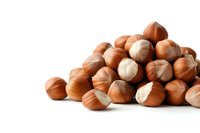 Fresh whole and cracked hazelnuts scattered on white background, organic raw nuts macro photography showing natural texture and details. Isolated food.