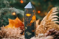 Crystal obelisk with golden inclusions surrounded by autumn decorative elements and bokeh lights creating magical atmosphere for spiritual practices.