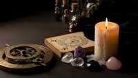 Mystical altar setup with burning candle, tarot cards, crystals, and occult symbols for spiritual divination and esoteric practices on dark wooden surface.