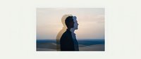 Young man with dark hair and South Asian appearance standing in profile against twilight sky with mountains, wearing dark jacket, contemplative mood for introspection and mindfulness concepts.