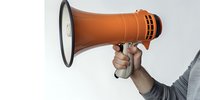Hand holding orange megaphone against light background, demonstrating announcement or public speaking concept, isolated with copy space for marketing use.
