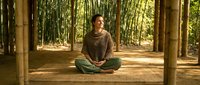 Young woman meditating in lotus position on wooden platform surrounded by bamboo forest. Peaceful zen moment for wellness and mindfulness practice.