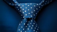 Close-up view of blue silk necktie with white polka dot pattern showing Windsor knot detail against dark background, suitable for business and fashion concepts.