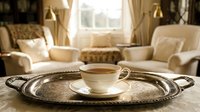 Elegant cream teacup and saucer on ornate silver tray in luxury living room with cream furniture and natural window light, suitable for home decor and lifestyle design.