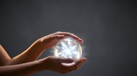 Hands protecting glowing crystal sphere with bright light rays emanating from center against dark background symbolizing energy protection and spiritual power.