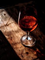Elegant wine glass filled with amber liquid on rustic wooden surface with dramatic lighting creating warm shadows and atmospheric mood for luxury dining.
