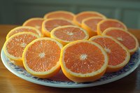 Fresh juicy orange slices arranged on decorative plate showing vibrant citrus flesh and natural segments, macro food photography in natural lighting.