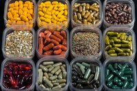 Colorful dietary supplements and vitamins in plastic containers arranged in rows, showing variety of capsules, pills and tablets in different colors and sizes.