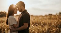 Romantic couple embracing in golden wheat field during sunset, intimate moment with warm sunlight creating dreamy atmosphere for wedding and love concepts.