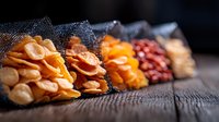 Assorted dried fruits and nuts in mesh bags arranged on rustic wooden surface, selective focus on colorful healthy snacks creating appetizing composition.