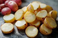 Fresh sliced baby potatoes with golden skin and creamy white flesh arranged on dark surface, macro food photography showing texture and natural lighting.