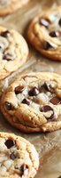 Fresh baked chocolate chip cookies on parchment paper with melted chocolate morsels, showing soft chewy texture and golden brown edges. Close up macro view.