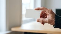 Senior man with light skin tone holding blank white business card in office environment, suitable for corporate branding, networking, and professional identity concepts.