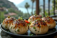 Steamed Asian dumplings garnished with sesame seeds, chives and spices on black plate against mountain landscape background. Fresh dim sum appetizers.