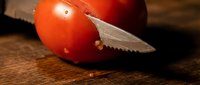 Ripe red tomato sliced with sharp knife on wooden cutting board, fresh produce for cooking and meal preparation.