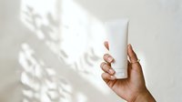 Unbranded cosmetic tube held by hand with warm skin tone against white background with natural shadow overlay.