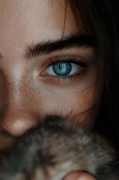 Close-up of bright blue eye with natural freckles and dark eyebrow. Partial face view showing intense gaze and delicate eyelashes against dark hair strands.