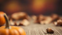 Autumn harvest scene with orange pumpkins and acorns on rustic wooden table with warm bokeh background for seasonal decorating and fall themes.