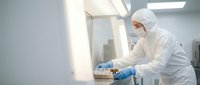 Laboratory technician in protective suit conducting scientific research in sterile cleanroom environment for pharmaceutical manufacturing and quality control.