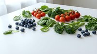 Fresh organic vegetables and berries arranged on white marble surface including broccoli, cherry tomatoes, spinach leaves and blueberries for healthy eating.