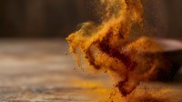 Vibrant golden powder explodes in dynamic motion against neutral background, creating swirling dust clouds and particles. Suitable for creative projects and design work.