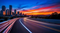 Long exposure highway with vibrant sunset sky and illuminated city skyline in background, capturing motion blur of vehicle light trails on curved road at dusk.