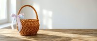 Empty wicker basket with white ribbon bow on wooden table near window with natural sunlight for Easter holiday decoration and gift presentation.