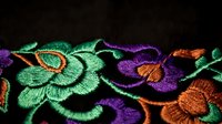 Colorful embroidered floral pattern with green and purple flowers on black fabric. Traditional needlework craft design for textile and fashion projects.