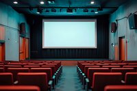 Empty modern cinema auditorium with red seats and blank white screen. Dark interior with turquoise walls and theatrical lighting creates atmospheric movie theater ambiance.