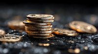 Stack of golden coins on dark textured surface with scattered money in blurred background for financial investment and wealth accumulation concepts.