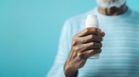 African American senior holding white medicine bottle against turquoise background, healthcare concept for elderly patients and medication management.