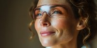 Close-up portrait of smiling woman with curly hair wearing protective glasses, illuminated by warm side lighting against dark background.
