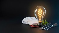 Vintage Edison bulb glowing warmly beside elegant table setting with white napkin and silverware on dark background for dining concepts.