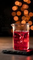 Glass beaker with red chemical solution on slate surface against warm bokeh lights background for laboratory research and scientific experiments.