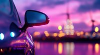 Side mirror of black car reflecting city lights at dusk with purple sky and bokeh effect. Urban nightscape with water reflections creates dreamy atmosphere.