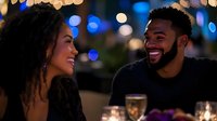 Young woman and man of mixed ethnicity enjoying evening conversation at outdoor venue with illuminated bokeh lights in background, holding glasses of champagne or wine, smiling and engaged in social interaction at night event or celebration.