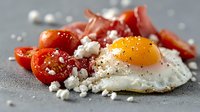 Sunny side up egg with cherry tomatoes, crumbled feta cheese and crispy bacon on gray background. Black pepper seasoning adds gourmet appeal.
