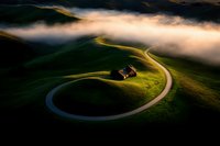 Winding mountain road through green hills with dramatic fog and golden sunrise light creating atmospheric landscape scenery for travel and nature concepts.