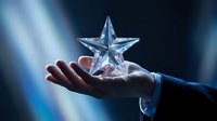 Male hand in business suit holding crystal star award against blue light rays background, symbolizing achievement and success.