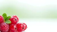 Fresh red currants and raspberries with mint leaf on soft green background for healthy eating and summer fruit concepts.