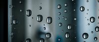 Water droplets on glass surface creating abstract pattern with blurred background. Natural condensation effect for modern design projects and textures.