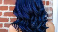 Vibrant blue hair with loose curls and waves styled in modern fashion look against brick wall background for beauty and hair color inspiration.