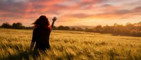 Woman with long dark hair waving in golden wheat field at sunset, enjoying nature and freedom outdoors.