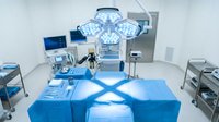 Modern operating room with surgical lights and medical equipment ready for procedure. Clean sterile environment with blue surgical table and advanced technology.