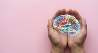 Protective hands cradling colorful brain model representing mental health awareness, psychology care, and neurological wellness on pink background.