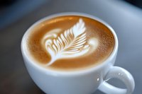 Delicate leaf pattern created in coffee foam shows expert barista skills, with rich brown and white contrast in ceramic cup against dark background.