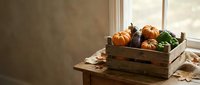 Autumn harvest vegetables in rustic wooden crate on farmhouse table by window with warm natural light creating cozy seasonal atmosphere for cooking.