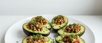 Halved avocados topped with seasoned ground meat, diced vegetables, and fresh herbs served on white plate for healthy meal prep and nutritious lunch ideas.