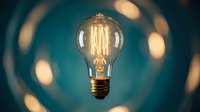 Vintage Edison light bulb with glowing filament against teal background with warm bokeh lights creating atmospheric lighting for creative projects.