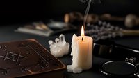Mystical candle flame illuminates ancient spell books and crystal formations on dark wooden table creating atmospheric occult scene for spiritual practices.